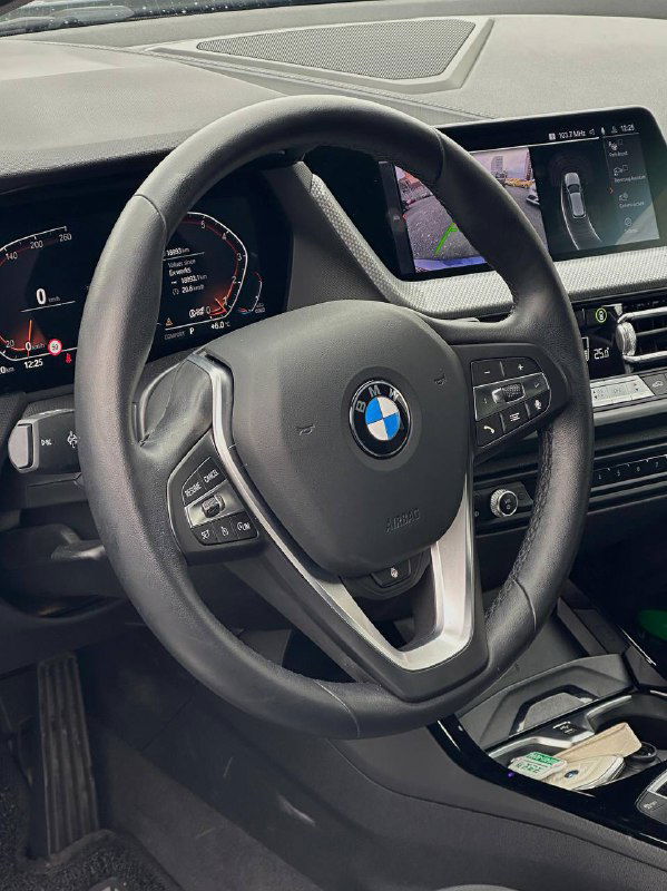 Салон BMW 120i: рулевое колесо с эмблемой BMW, мультифункциональные кнопки и часть приборной панели, чистый интерьер.