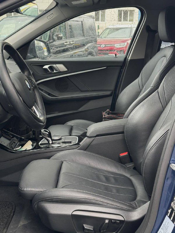 Передние сиденья BMW 120i в чёрной коже, вид под углом на кресло водителя и пассажирское сиденье, чистое состояние салона.