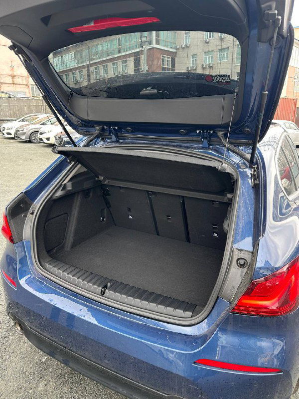 Открытый багажник BMW 120i с выраженной вместимостью, вид сзади на дифрагму багажного отделения и складные спинки сидений.