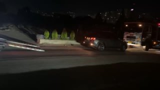 Кадр ночной съёмки: автомобиль въезжает на автовоз при искусственном освещении, видны рабочие и оборудование на фоне.