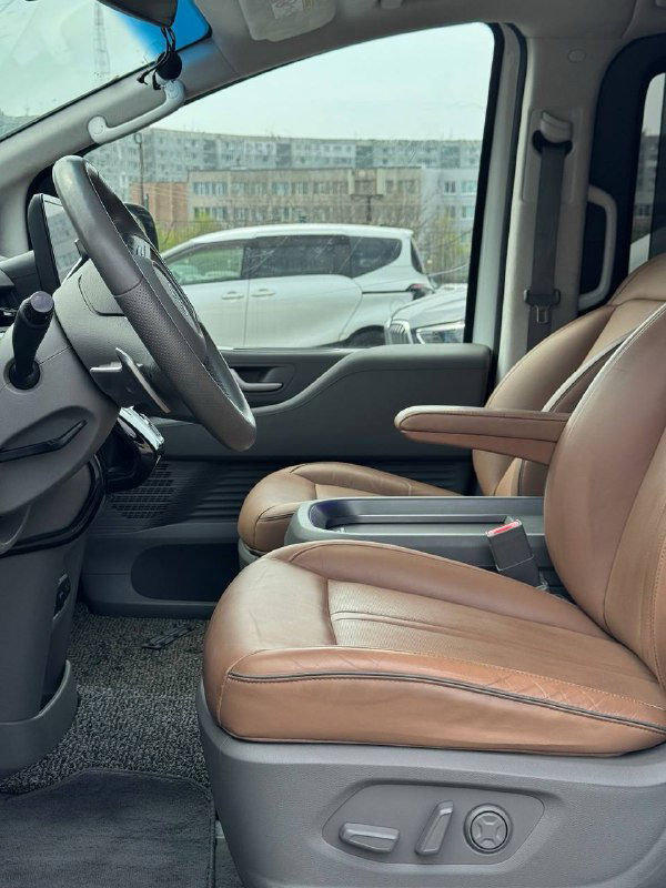 Передние кожаные кресла Hyundai Staria в бежевой/коричневой отделке, вид сбоку с панорамой салона и подлокотниками.