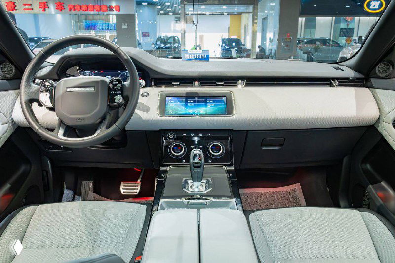 Интерьер Range Rover Evoque 2021 другой комплектации: вид на переднюю панель, мультимедийный дисплей и центральный тоннель, салон в светлой отделке.