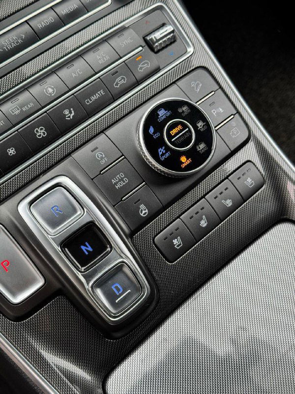 Крупный план центральной панели управления и шайбы селектора передач у Hyundai Santa Fe с кнопками режима движения и парковки.