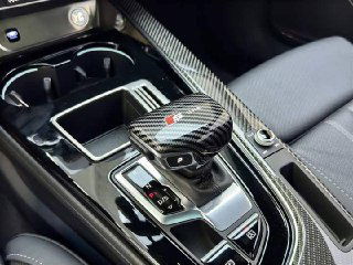 Детальный кадр центральной консоли Audi A4L: селектор коробки передач, отделка под карбон, подстаканники и элементы управления климатом вблизи.