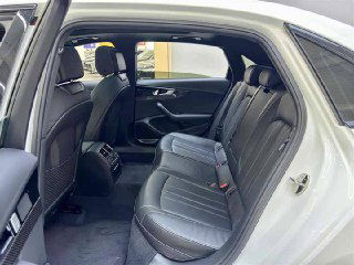 Задний ряд салона Audi A4L: три посадочных места, кожаная обивка и комфортный простор для пассажиров, виден второй ряд на фоне освещённого шоурума.