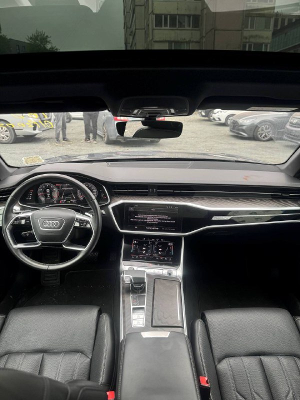Вид салона Audi A6 с водительского места: панорамный обзор торпеды, рулевого колеса и центральной консоли с мультимедийными экранами в интерьере.