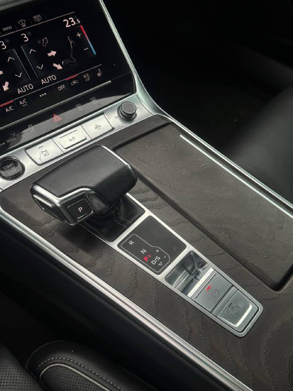 Крупный план рычага коробки передач и центрального туннеля Audi A6 с отделкой и управляющими кнопками рядом, обзор зоны для хранения.