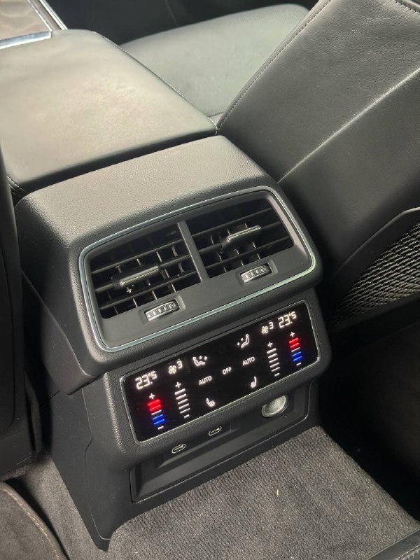 Крупный план блока климат-контроля для задних пассажиров Audi A6 с цифровыми индикациями температуры и вентиляции, вид на консоль между сиденьями.