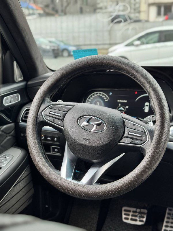 Рулевое колесо Hyundai Palisade с органами управления и логотипом, вид на панель приборов и часть водительского места в интерьере.