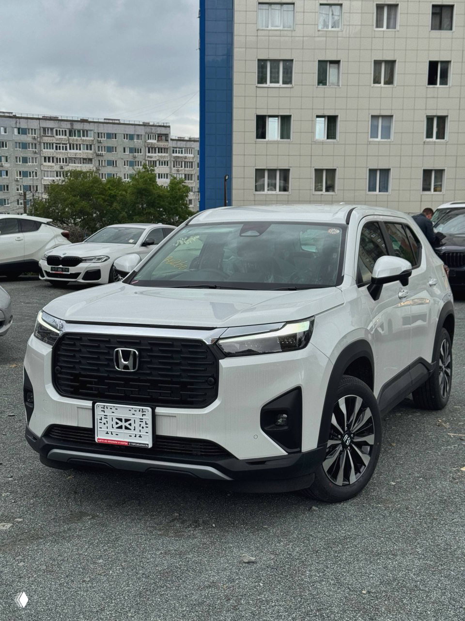 Фронтальный вид белого Honda WR‑V на стоянке: крупная решётка радиатора, фары и временный номер на переднем бампере.