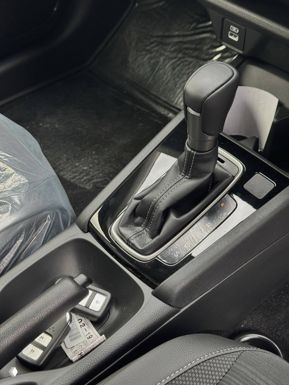 Крупный план кулисы автоматической коробки передач, ручного тормоза и ключей на центральной консоли белого Honda WR‑V.