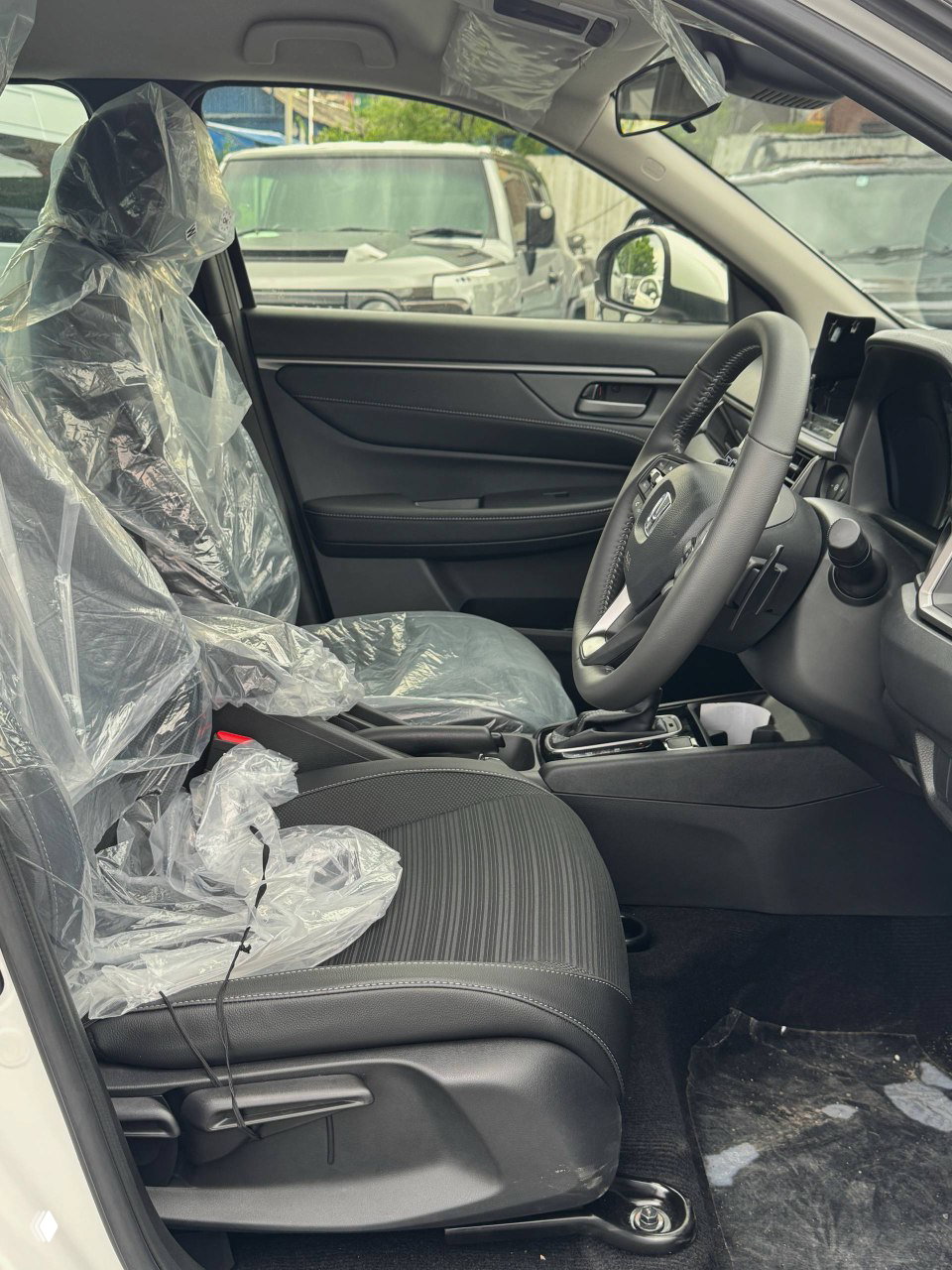 Переднее сиденье внутри нового Honda WR‑V закрыто защитной плёнкой, вид на водительское и пассажирское место в салоне.