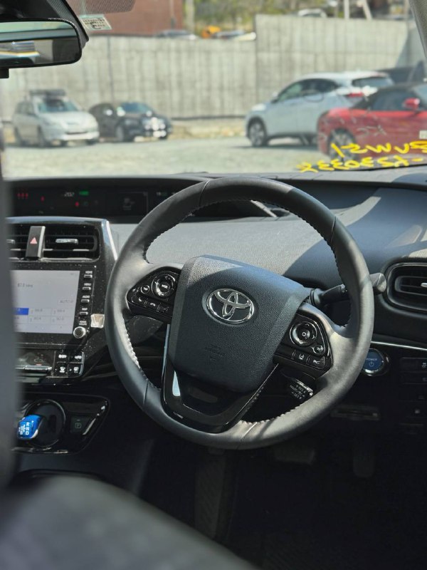 Салон Toyota Prius: вид на рулевое колесо, панель приборов и мультимедийную систему с логотипом Toyota на руле.