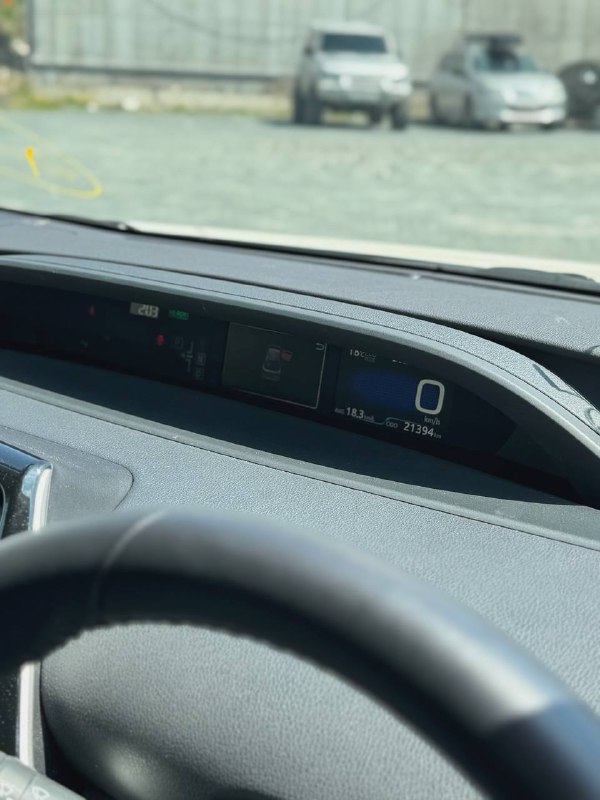 Приборная панель Toyota Prius: цифровые показатели скорости и индикаторы гибридной системы, вид частично в фокусе через руль.