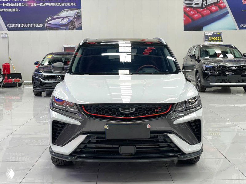 Фронтальный вид белого Geely Coolray 2022 в шоуруме — подробный снимок передней части, фары и решетка с красной окантовкой, на фоне другие автомобили.