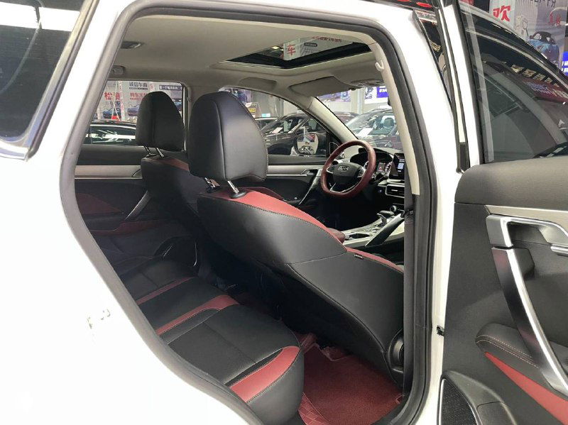Интерьер Geely Coolray: задний ряд сидений с черной и красной отделкой, вид через открытую заднюю дверь демонстрирует состояние обивки и пространства для ног.