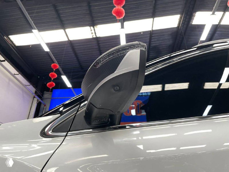 Боковое зеркало и крыша белого Geely Coolray в шоуруме — снимок показывает зеркальную конструкцию и внешний вид корпуса с отражением освещения зала.