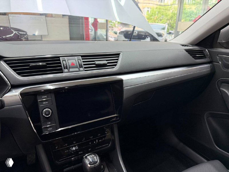 Ближний план центральной консоли Skoda Superb с мультимедиа и климат-контролем, видно состояние пластика и экран.