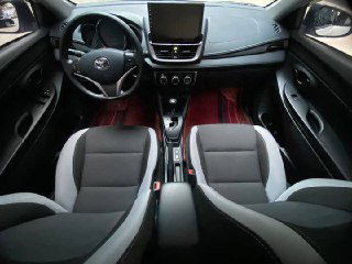 Салон Toyota Yaris L: передние сиденья, торпеда и руль в хорошем виде; показано общее состояние интерьера и материалы отделки.