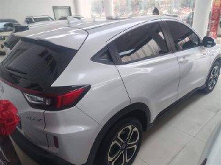 Боковой ракурс белого Honda XR-V (Vezel) в шоу-руме: видно профиль кузова, колёсные диски и задние фары, автомобиль на выставочном полу.