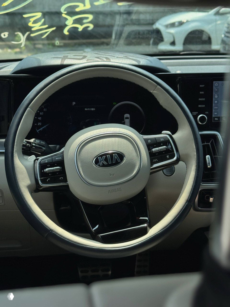Рулевое колесо KIA с логотипом Kia, элементы управления на руле и часть приборной панели, вид из водительского места.