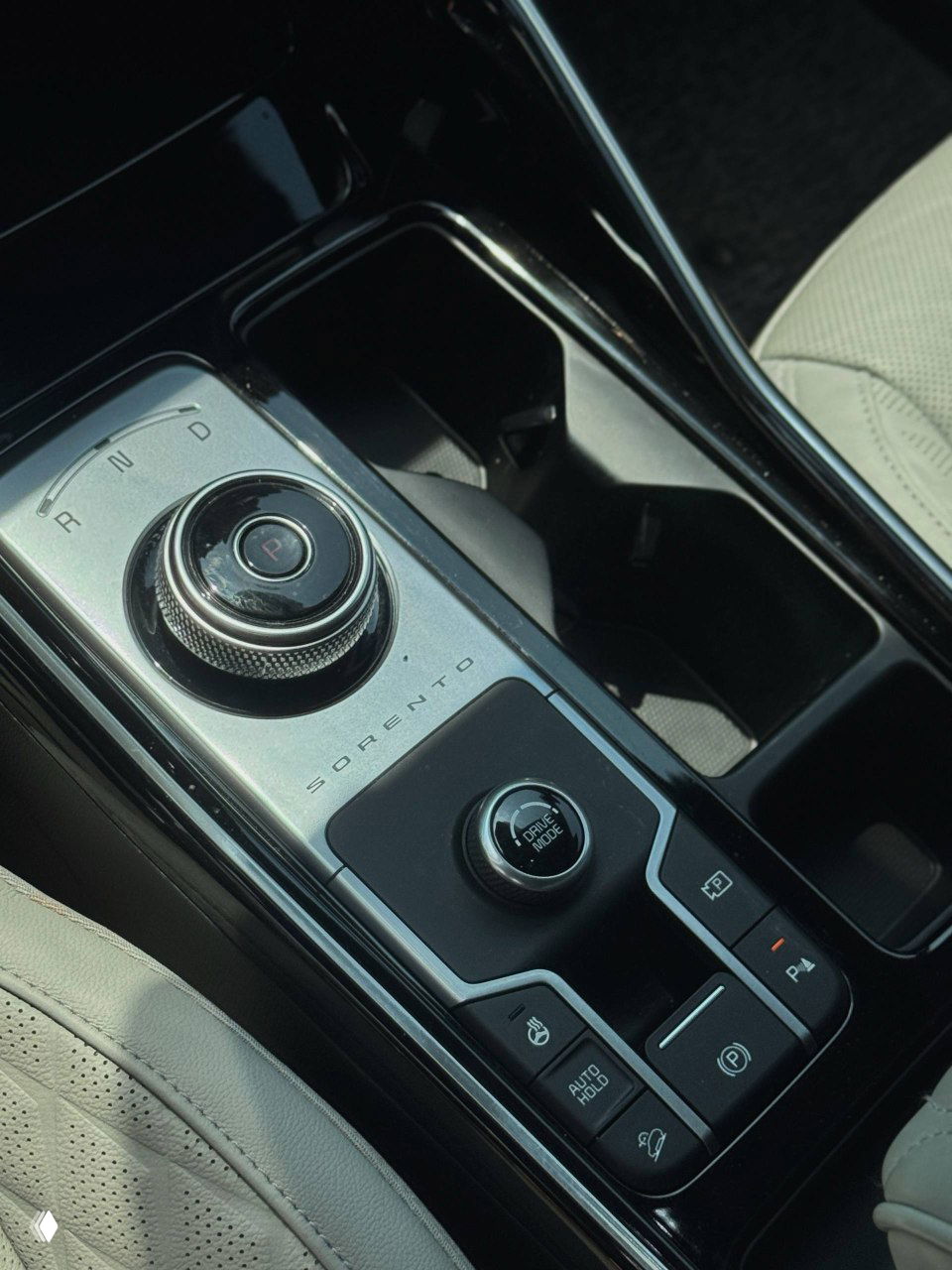 Крупный план селектора передач и блока управления в центральной консоли KIA Sorento, видна надпись 'SORENTO' на металлосетке.