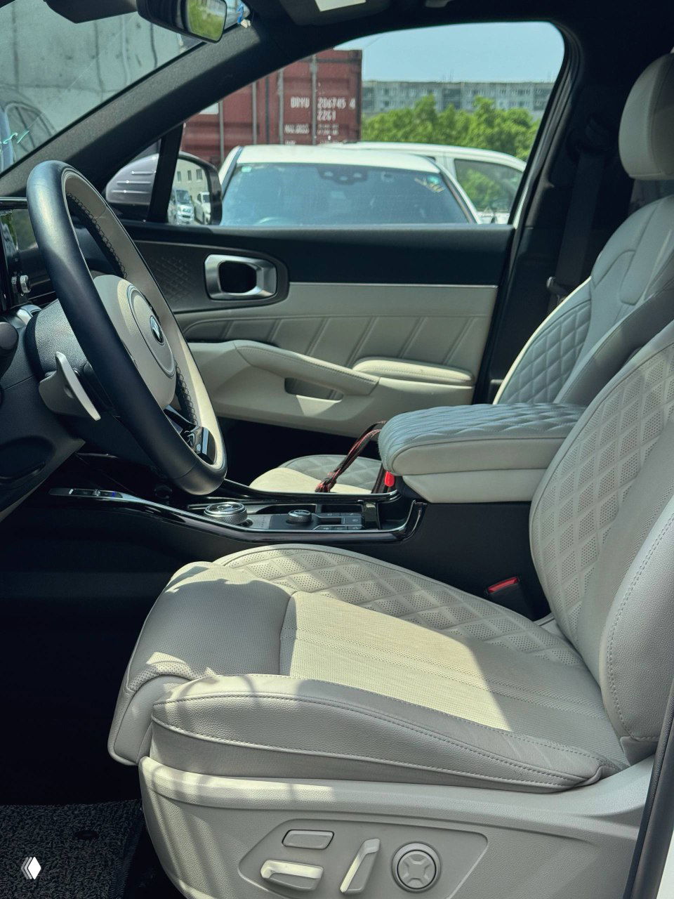 Передние сиденья KIA Sorento в светлой обивке, вид на водительское кресло и центральный подлокотник, показано положение регулировок.