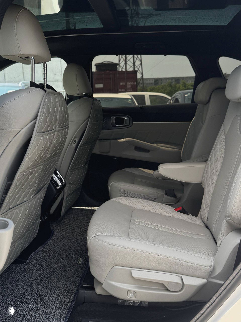 Второй ряд сидений KIA Sorento — два отдельных кресла со светлой обивкой и откидывающимся подлокотником, вид с боковой двери.