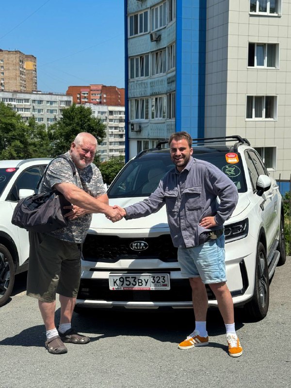 Рукопожатие менеджера и клиента на фоне Kia Sorento при выдаче автомобиля: официальное завершение сделки и обмен приветствиями перед отъездом.
