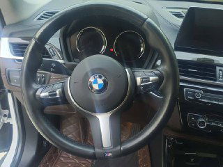 Крупный план рулевого колеса BMW X1 xDrive 25Li 2021 — руль с логотипом BMW, органы управления на подрулевых клавишах и вид приборной панели.