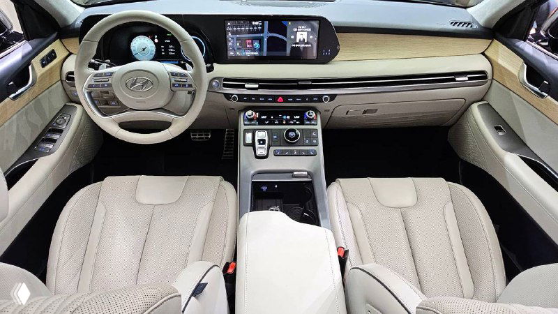 Салон Hyundai Palisade 2022 бежевого цвета — широкий панорамный вид на руль, центральную консоль и посадочные места переднего ряда с отделкой.