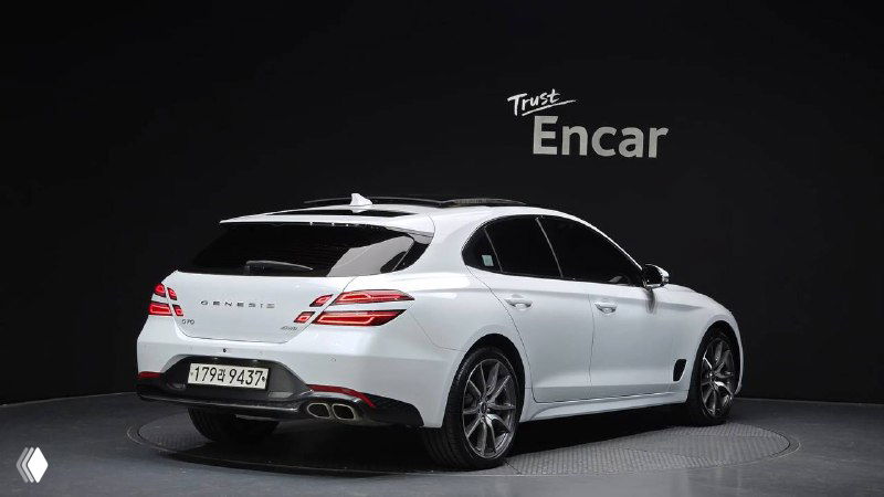 Вид сзади на белый Genesis G70: багажник, фонари и двойной выхлоп на фоне стенда Trust Encar — фото комплектации и состояния кузова.