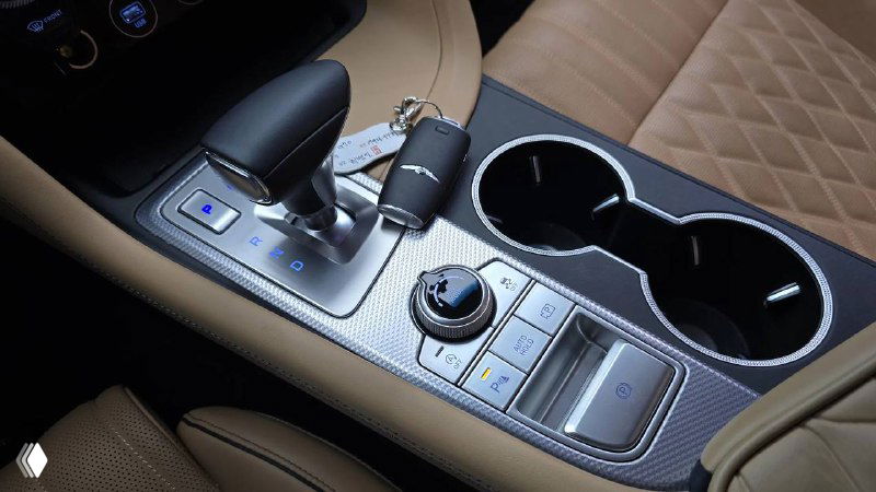 Блок селектора передач и управляющие кнопки на центральной консоли Genesis G70, отделка металлом и кожаные вставки рядом с подстаканниками.