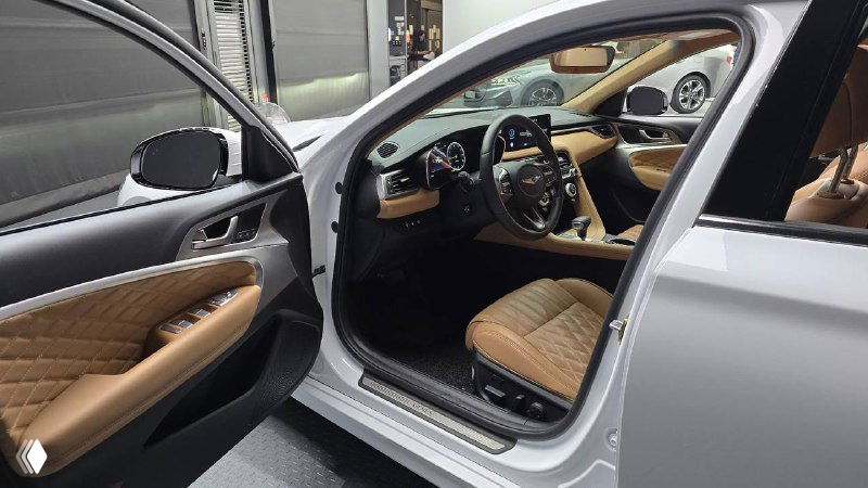 Открытая передняя дверь Genesis G70 и вид на переднее кресло с бежевой отделкой, порог и внутренняя отделка двери крупным планом.