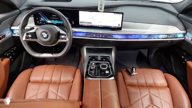 Салон BMW 740d с коричневыми кожаными сиденьями, общий ракурс центральной консоли, приборной панели и передних кресел без пассажиров.