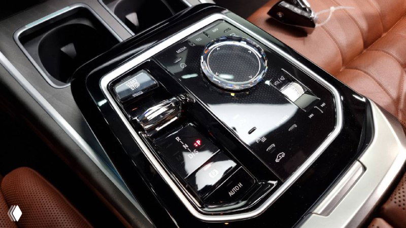 Крупный план декоративной панели и контроллера в центральной консоли BMW 740d; элементы управления и хромированные вставки на фоне кожаной обивки.