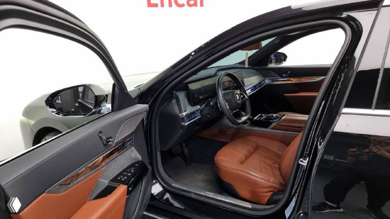 Открытая передняя дверь BMW 740d — вид на водительское место и часть салона с коричневой кожей, ракурс со стороны улицы/стенда.