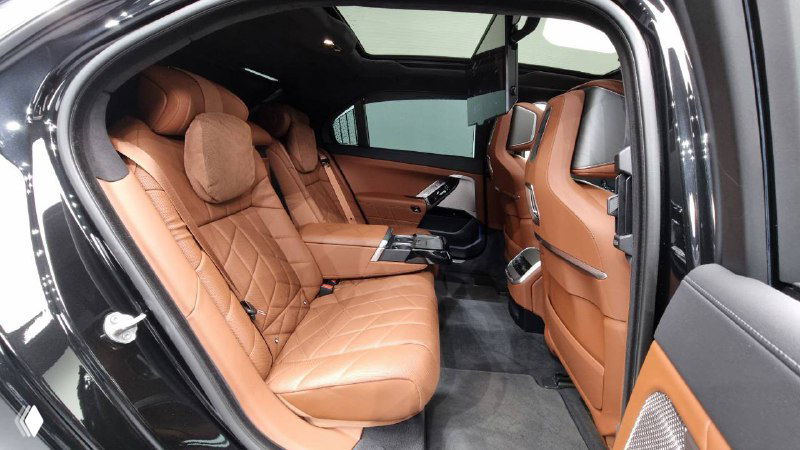 Задний ряд сидений BMW 740d с коричневой кожей; вид на большой монитор, установленный для пассажиров второго ряда и площадку между креслами.