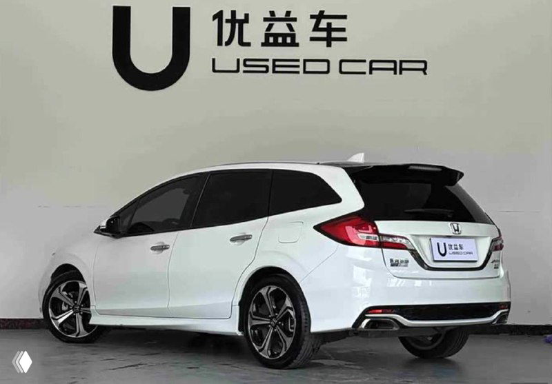 Белая Honda Jade, вид сзади-слева в шоуруме; видны задняя оптика, бампер, стильные диски и общая форма хэтчбека в дилерской обстановке.