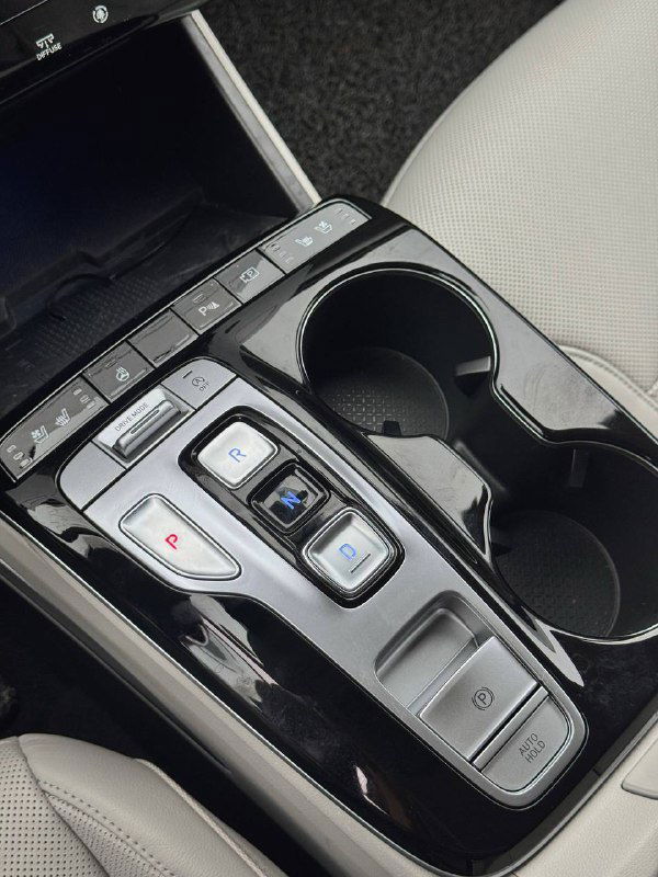 Фотография центральной консоли и селектора трансмиссии Hyundai Tucson: кнопочный селектор, подстаканники и отделка вокруг рычага управления АКПП.