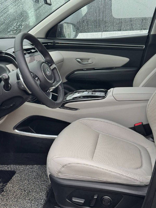 Фото передних кресел и центральной части салона Hyundai Tucson: светлая обивка сидений, подлокотник и декоративные элементы интерьера с боку.