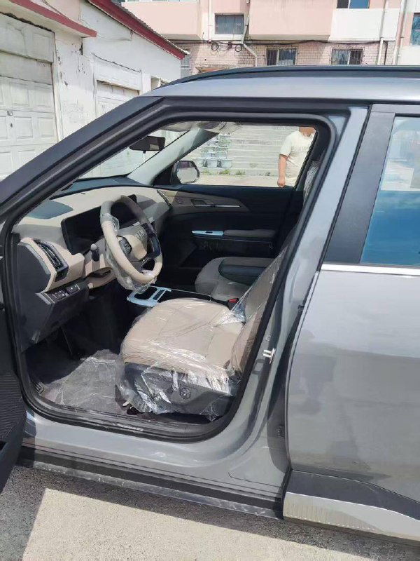 Открытая передняя дверь KIA EV5: вид на салон, водительское кресло в упаковке и панель приборов нового электромобиля.