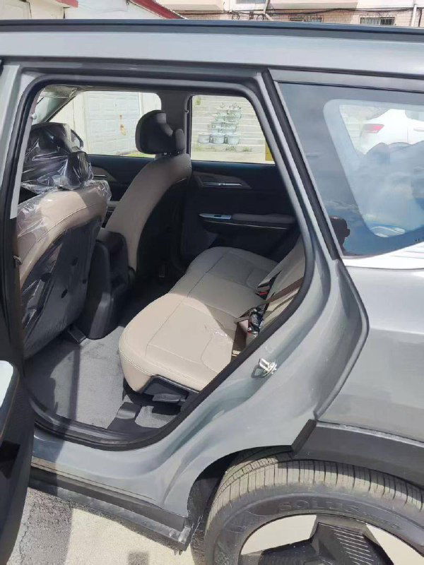 Вид через открытую заднюю дверь KIA EV5 на задний ряд сидений: новые бежевые сиденья и пространство для пассажиров.