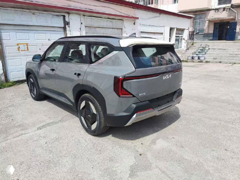 Задняя часть серого KIA EV5: общий вид сзади с логотипом KIA и светодиодной оптикой на стоянке перед отправкой.