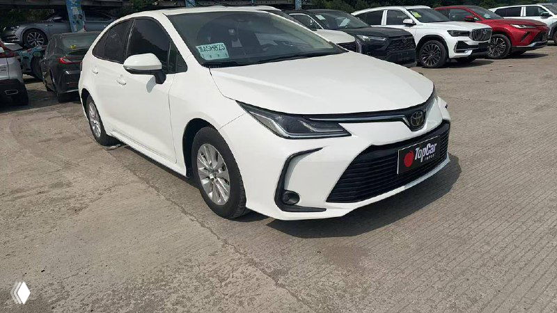 Toyota Corolla 2022, общий вид спереди справа; белый кузов, выразительная решётка и фары, автомобиль на площадке вместе с другими импортируемыми машинами.