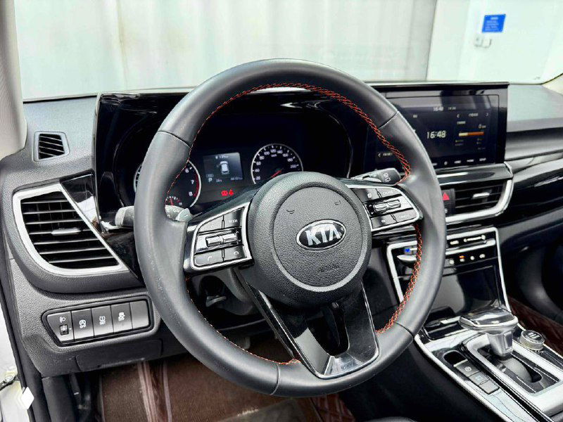 Рулевое колесо KIA с крупным планом: мультируль, подрулевые кнопки и декоративная прострочка на кожаной оплетке.