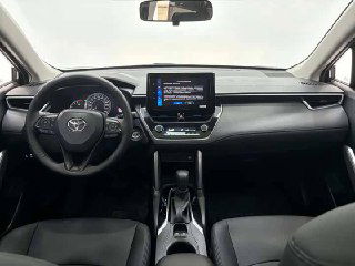 Салон Toyota Corolla Cross: панель приборов, мультимедиа‑экран и рулевое колесо в чёрной отделке — интерьерный вид с передних сидений.