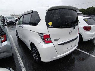 Вид сзади белого Honda Freed 2014 на автоплощадке: открытую заднюю часть видно в общей колонке машин, задние фонари и шильдик FREED отчетливо видны.