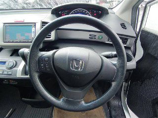 Салон: снимок рулевого колеса и панели приборов белого Honda Freed 2014, вид на центральную консоль с навигацией и рулевыми элементами управления.