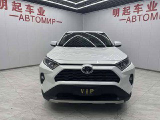 Фронтальный крупный план белого Toyota RAV4 в автосалоне: центральная решетка, фары и номерной знак «VIP», отражения потолочной подсветки на капоте.